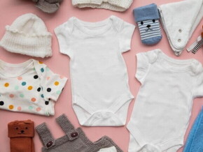Roupas de bebê diversas, dispostas sobre uma superfície rosa.