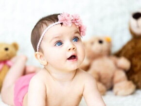 Um bebê deitado com a boca aberta, com ursos de pelúcia ao fundo.