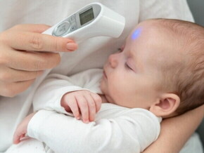 Uma mão medindo a temperatura do bebê com termômetro digital na testa.