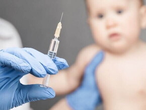 Mão com luva cirúrgica segurando seringa com a vacina da coqueluche, enquanto bebê aguarda a aplicação Mão com luva cirúrgica segurando seringa com a vacina da coqueluche, enquanto bebê aguarda a aplicação