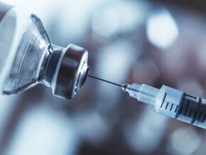 Imagem de uma seringa de vacina e um frasco de medicamento sob um fundo desfocado