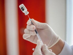 Profissional de saúde com luvas preparando uma seringa com uma dose de vacina retirada de um frasco.