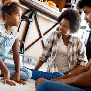 Pai e mãe estão sentado nos chão e conversam com sua filha, uma criança de 5 anos. Pai e mãe estão sentado nos chão e conversam com sua filha, uma criança de 5 anos.