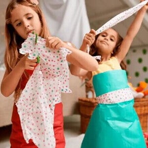 Duas crianças de cerca de 8 anos cortam papel colorido com uma tesoura sem ponta customizando pequenas peças de roupa com este material. Uma delas está utilizando, sobre a sua roupa comum, um vestido feito de papel. Duas crianças de cerca de 8 anos cortam papel colorido com uma tesoura sem ponta customizando pequenas peças de roupa com este material. Uma delas está utilizando, sobre a sua roupa comum, um vestido feito de papel.