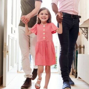 Uma menina com aspecto de felicidade, andando de mãos dadas com dois homens em um ambiente doméstico.