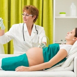 Médica realizando o procedimento de amniocentese em uma gestante deitada, utilizando uma agulha fina para coletar amostra do líquido amniótico. Médica realizando o procedimento de amniocentese em uma gestante deitada, utilizando uma agulha fina para coletar amostra do líquido amniótico.
