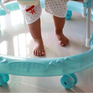 Pés de um bebê em um andador azul, sobre piso claro, mostrando o equipamento em uso. Pés de um bebê em um andador azul, sobre piso claro, mostrando o equipamento em uso.