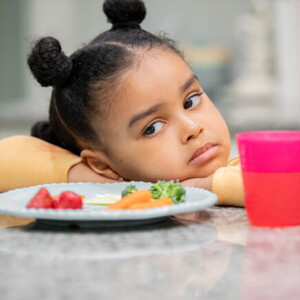 menina com semblante desconfiado olha para prato de comida sem vontade