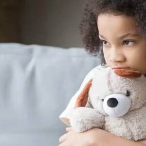 Imagem de uma criança sozinha segurando um bicho de pelúcia, olhando de forma distraída para o nada, este olhar pode ser um sintoma de síndrome de asperger