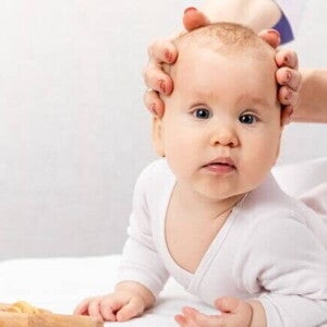 Um bebê deitado com a sua cabeça sendo segurada por duas mãos