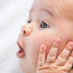 Um close-up do rosto de um bebê, com a boca ligeiramente aberta e a mão levantada perto do rosto. Um close-up do rosto de um bebê, com a boca ligeiramente aberta e a mão levantada perto do rosto.