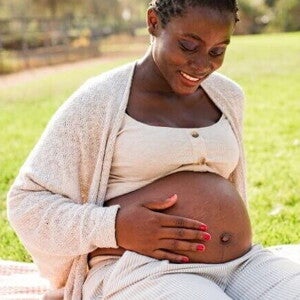 Mulher grávida sorrindo sentada na grama e acariciando a barriga