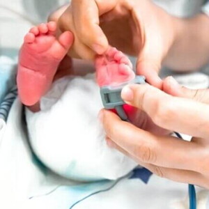 Pés de um bebê recém-nascido passando por uma avaliação pelas mão de um profissional da saúde.