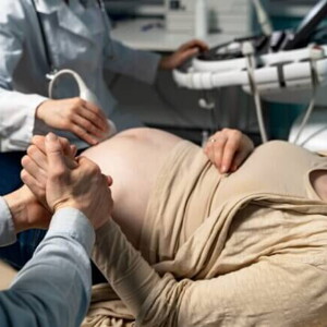 Uma gestante deitada em um consultório médico, segurando a mão de um homem, durante um exame de ultrassom