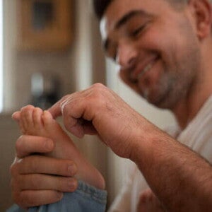 Um homem sorrindo e segurando o pé de uma criança fazendo um movimento de cócegas com o dedo.