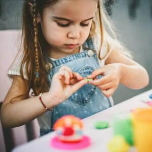 A foto mostra uma criança brincando de massinha de modelar e estimulando a coordenação motora fina