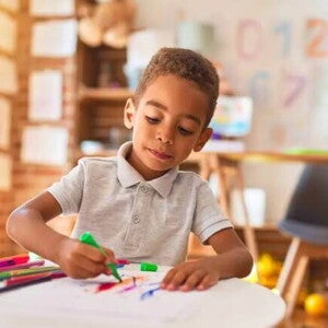 Uma criança de 4 anos está em uma sala de aula, sentado à mesa, e usa uma caneta hidrocor para desenhar Uma criança de 4 anos está em uma sala de aula, sentado à mesa, e usa uma caneta hidrocor para desenhar