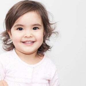 Bebê sorrindo, vestindo uma roupa rosa em um fundo branco.