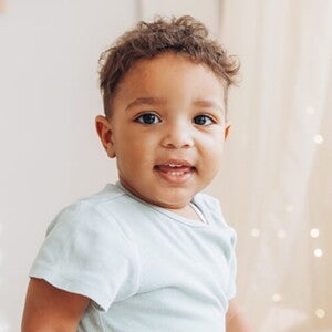 Criança vestindo blusa azul claro em um quarto de cores neutras e luzes de decoração