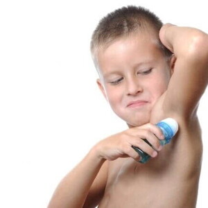 Menino utilizando um desodorante em formato roll-on sob um fundo branco.