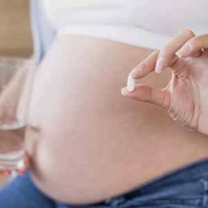 Mulher grávida segurando um copo de água em uma mão e uma cápsula de suplemento na outra mão Mulher grávida segurando um copo de água em uma mão e uma cápsula de suplemento na outra mão