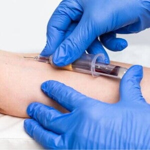 Profissional usando luvas azuis realizando coleta de sangue no braço de uma pessoa com uma seringa. Profissional usando luvas azuis realizando coleta de sangue no braço de uma pessoa com uma seringa.