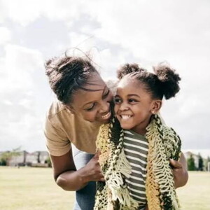 Mãe e filha rindo abraçadas em um campo de futebol