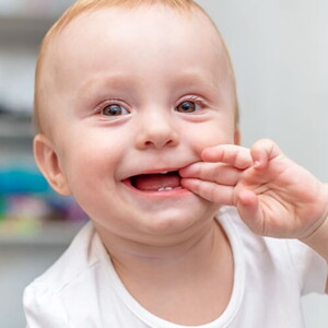 Bebê engatinhando no chão e com a mão na boca sorrindo.