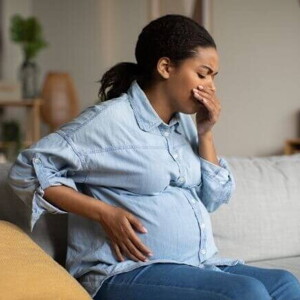 Mulher grávida sentada em um sofá, com uma mão na barriga e a outra mão na boca.