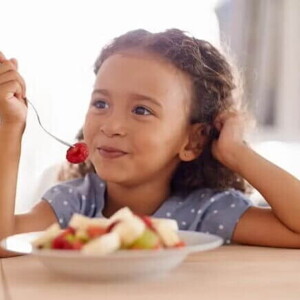 Representando bons hábitos alimentares, uma criança come seu lanchinho: várias frutas picadas em um prato. 