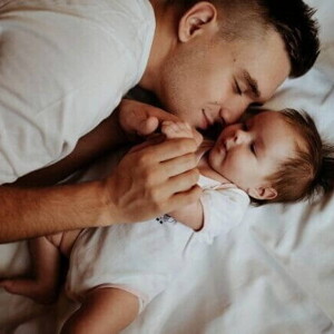 Homem deitado com um bebê em uma cama.