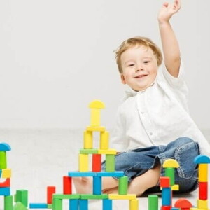 Um bebê sentado no chão com a mão para cima, em frente de diversos blocos coloridos de construir.