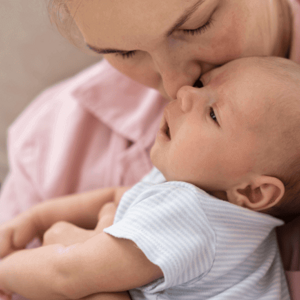 Mãe segurando no colo bebê recém nascido e beijando sua testa.