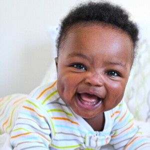 Bebê deitado e sorrindo, deitado em uma cama, sob um fundo branco.