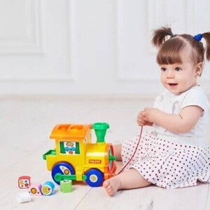 Bebê sentada no chão segurando um trenzinho de brinquedo