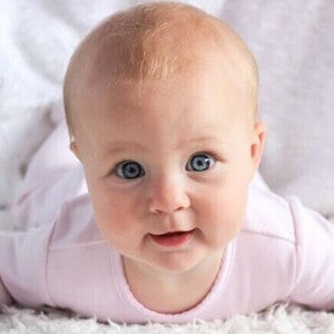 Bebê de olhos claros e roupa cor de rosa olhando fixamente para a câmera.