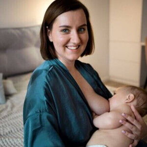 Uma mãe sorrindo, sentada, amamentando um bebê em seu colo
