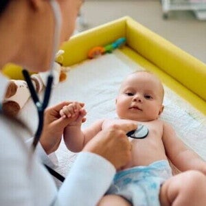 Um bebê deitado sendo examinado por uma pediatra com um estetoscópio