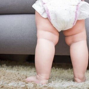 Imagem das pernas de um bebê em pé, em cima de um tapete