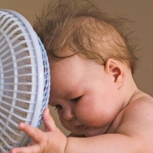 Um bebê com a cabeça próxima a um pequeno ventilador Um bebê com a cabeça próxima a um pequeno ventilador