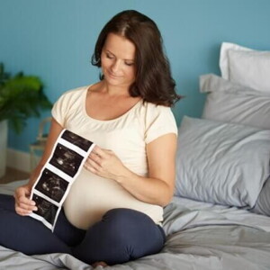 Mulher grávida sentada em uma cama, observando o resultado de um exame de ultrassom