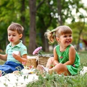 Piquenique infantil Um menino e uma menina estão sentados em uma toalha em um parque. Sobre ela temos algumas cestas e lanchinhos. O cenário todo remete muito a um dia de piquenique
