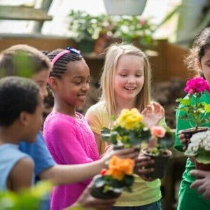 Um grupo de crianças em um jardim comunitário, segurando vasos de plantas coloridas e sorrindo enquanto participam de uma atividade de jardinagem.
