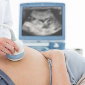 Mulher grávida deitada e sorrindo enquanto passa por um exame de ultrassom.