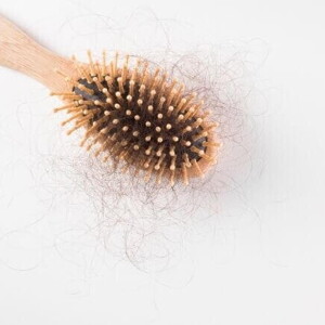 Uma escova de cabelo de madeira, com bastante cabelo preso aos seus dentes, sobre um fundo branco