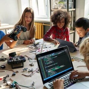 Grupo de crianças sentadas em uma mesa com várias ferramentas tecnológicas.