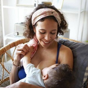 Mãe sentada e sorrindo, amamentando um bebê em seu colo Mãe sentada e sorrindo, amamentando um bebê em seu colo