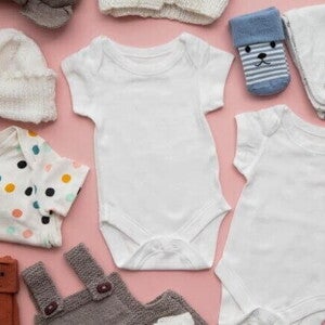 Roupas de bebê diversas, dispostas sobre uma superfície rosa.