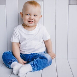 Um bebê sentado, sorrindo, veste uma camisa branca e uma calça jeans, sob um fundo branco. Um bebê sentado, sorrindo, veste uma camisa branca e uma calça jeans, sob um fundo branco.