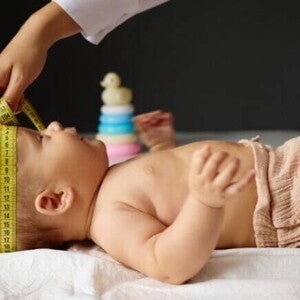 Um bebê deitado, com a cabeça sendo medida por outra pessoa com uma fita métrica. Um bebê deitado, com a cabeça sendo medida por outra pessoa com uma fita métrica.